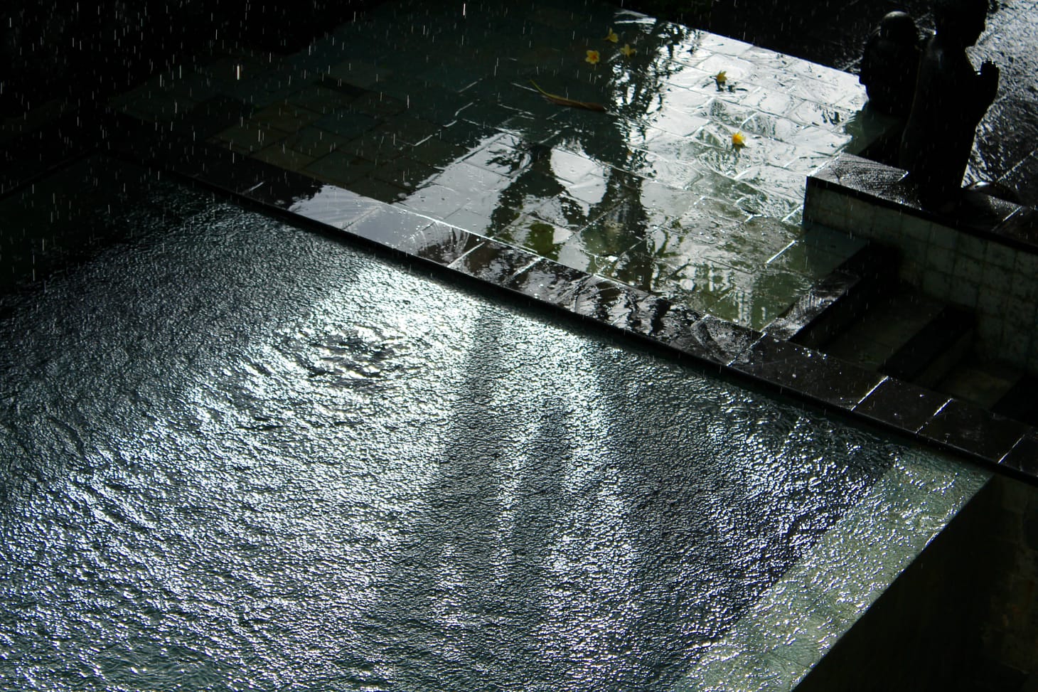 Rain falling into a swimming pool as sunlight hits the water.